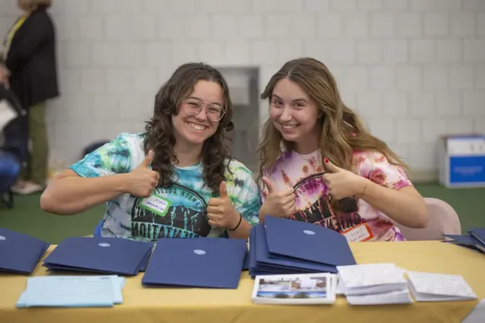 Two students smiling and giving thumbs-ups to the camera.