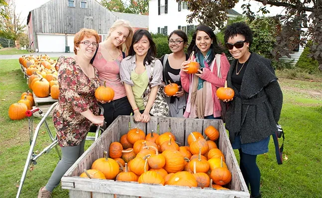 A group of Smith students visiting a pumpkin patch and posing holding pumpkins
