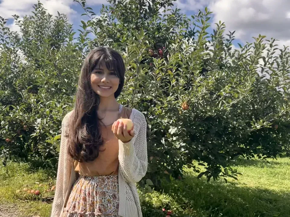 Gloria Parrales ’24, smiling, holds an apple in an orchard